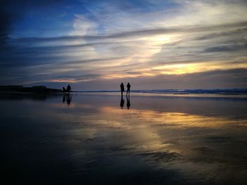 Silhouette people on beach against sky during sunset