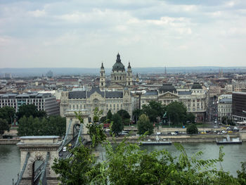 Chain bridge over danube river in city against cloudy sky