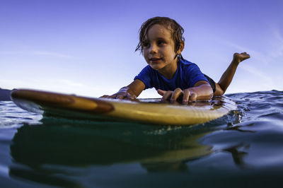 Close up of a 3 years old surfer floating on a wooden surfboard