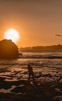 Silhouette person standing on beach against sky during sunset