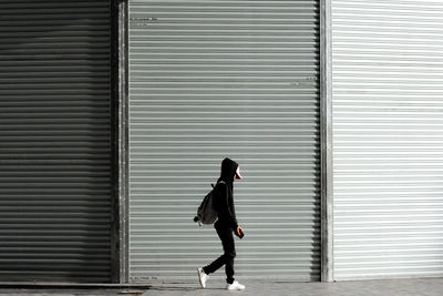 Side view of woman walking against closed shutter