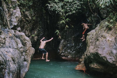 Rear view of kids jumping into rock pool