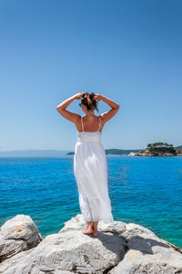 Man standing on rock by sea against clear sky