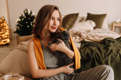 A pretty girl in pajamas rejoices and smiles during the christmas holidays in cozy bedroom interior