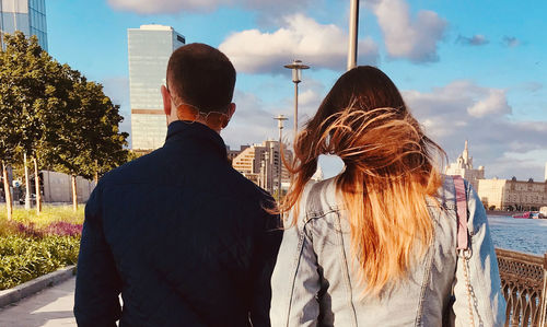 Rear view of friends standing against sky in city