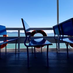 Empty chairs and table at beach against clear blue sky