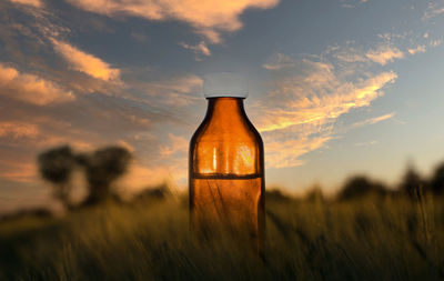 Close-up of beer bottle on field against sunset sky