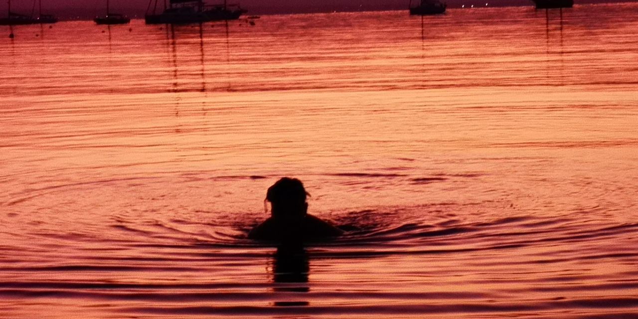 SILHOUETTE PERSON SWIMMING IN SEA AGAINST SUNSET SKY