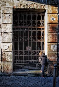 Rear view of boy wearing warm clothing peeking through gate in city