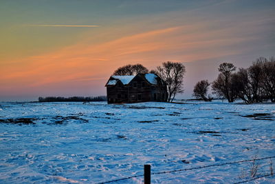Building by frozen lake against sky during sunset