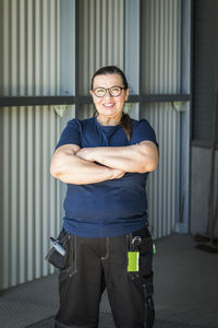 Portrait of smiling mature female worker standing with arms crossed on warehouse entrance