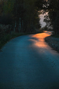 Road amidst trees in forest against sky at dusk