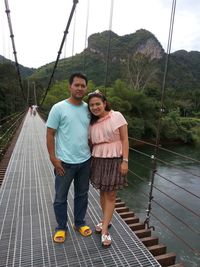 Full length portrait of couple standing over river on footbridge