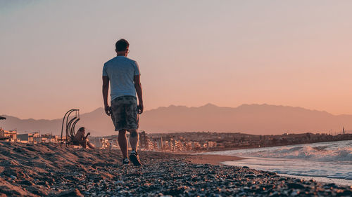 Rear view of man standing on land against sky during sunset