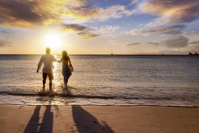 Rear view of woman standing at beach against sky during sunset