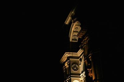 Low angle view of clock tower against building at night