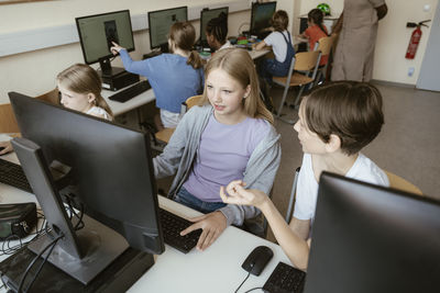 High angle view of male and female classmates discussing while sitting in computer class at school