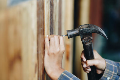 Cropped hands hammering nail in wooden wall