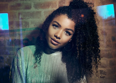 Portrait of beautiful woman with curly hair standing against wall