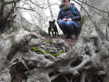 Portrait of woman crouching with french bulldog by trees
