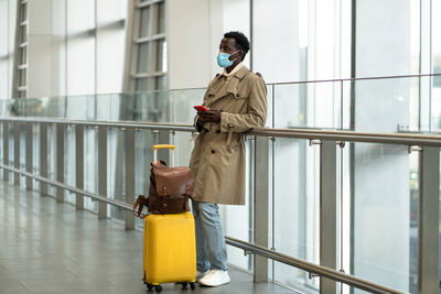 Afro traveler man stands in airport terminal, wear face mask, waiting for flight and boarding
