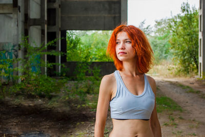 Thoughtful redhead woman looking away while wearing sports bra on land