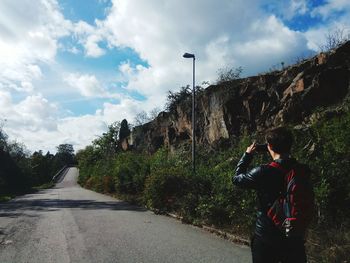 Rear view of man photographing on road against sky