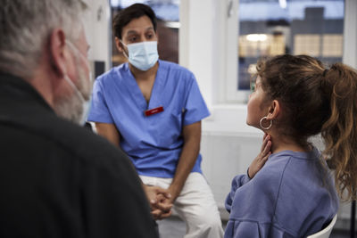 Male doctor talking to girl patient and grandfather during appointment