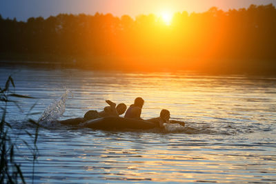 Silhouette people swimming in lake against sky during sunset