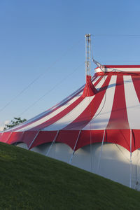 Low angle view of circus tent on field against clear blue sky