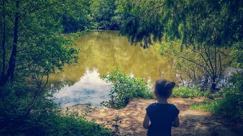 Rear view of girl standing by lake against trees