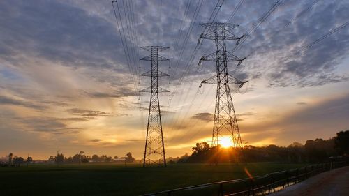 Silhouette electricity pylons on field against sky during sunset