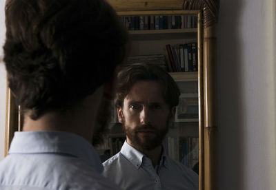 Rear view of confident young man reflecting on mirror at home