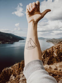 Cropped image of man hand with tattoo against lake