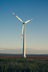 Windmill on field against clear blue sky