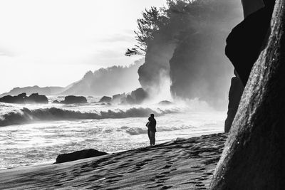 Man standing on rock by sea against sky