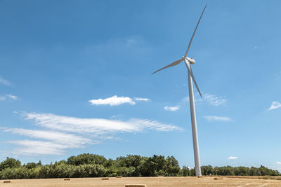 Single wind turbine in the middle of a field on a blue summer sky