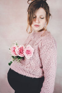 Close-up of woman with pink rose standing against wall