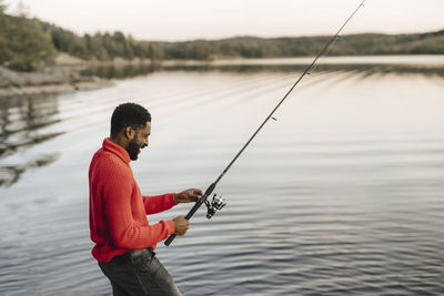 Smiling man fishing in lake during sunset