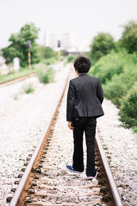 Rear view of man walking on railroad track