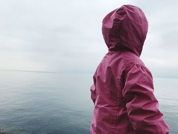 Rear view of baby girl wearing pink raincoat by sea against sky
