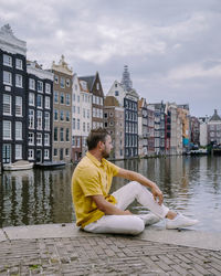 Man sitting by buildings against sky in city