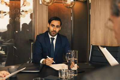 Portrait of confident mid adult lawyer with documents at conference table in law office