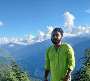 Young man wearing sunglasses standing on mountain against sky