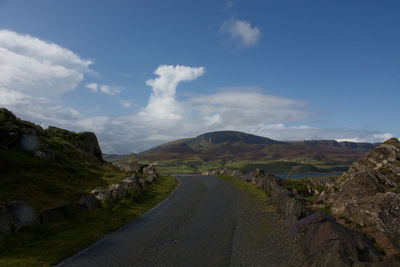 Empty road leading towards mountains against sky