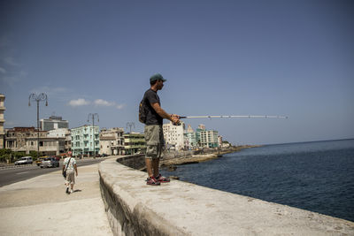 People on sea by city against sky