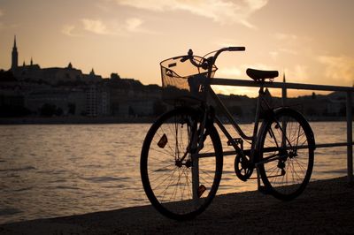 Bicycle parked on footpath by danube river against sky during sunset