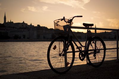 Bicycle parked on footpath by danube river against sky during sunset