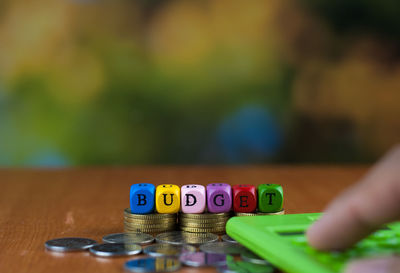 Close-up of hand using calculator by text made with toy blocks over coins on table