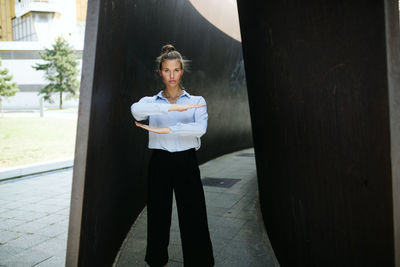 Portrait of young woman gesturing equal sign while standing amidst wall